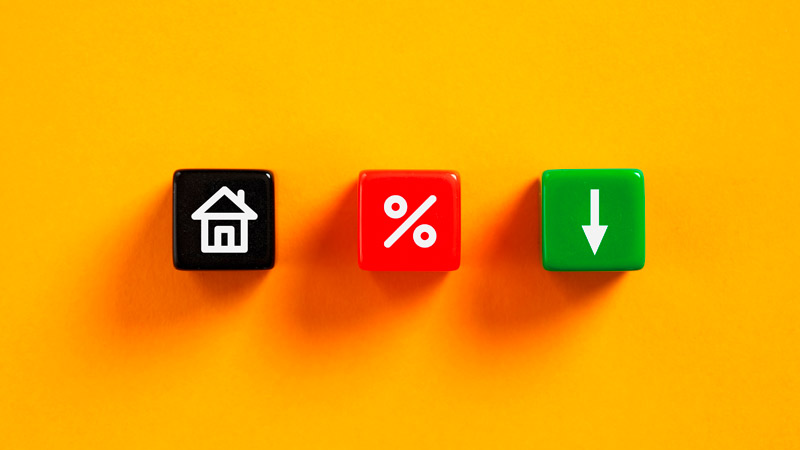 3 dados sobre um tampo amarelo: o primeiro tem um icone de uma casa; o segundo de uma percentagem e o terceiro uma seta a descer - alusão à descida dos juros